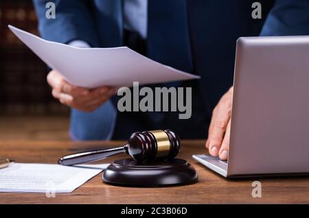 Mittelteil der Rechtsanwalt Holding Dokumente in der Nähe von Hammer und Laptop am Schreibtisch im Gerichtssaal Stockfoto