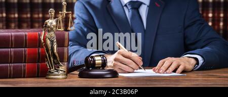 Mittelteil der Rechtsanwalt Signieren von Dokumenten in der Nähe von Hammer und Schuppen am Schreibtisch im Gerichtssaal Stockfoto