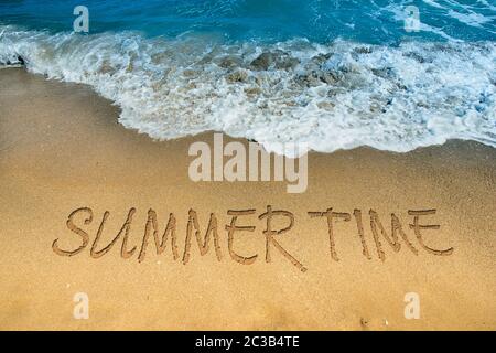 Welle des blauen Meeres am Sandstrand. Der Text Sommerzeit im Sand geschrieben. Erstaunlich schöne Meereslandschaft mit Sommerwort Inschrift auf dem Meer Stockfoto