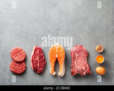 Carnivore oder Keto Diät Konzept. Rohe Zutaten für Null-Carb-oder Low-Carb-Diät - Burger Patties, Ribeye, Lachssteak, Schweinefleisch, Ei auf grauen Stein Backgro Stockfoto