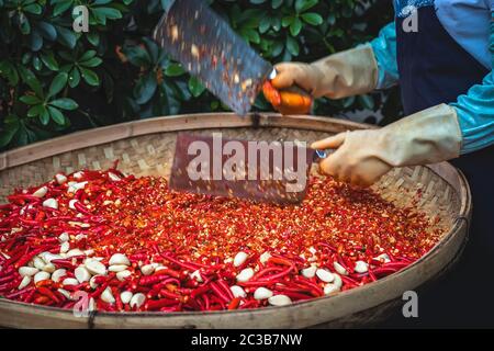 Chilis und Knoblauch werden von der Arbeiterinnen in einer Korbschale auf dem Straßenmarkt in Yangshuo, China, gehackt Stockfoto