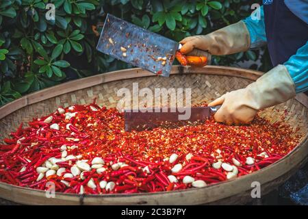 Chilis und Knoblauch werden von der Arbeiterinnen in einer Korbschale auf dem Straßenmarkt in Yangshuo, China, gehackt Stockfoto