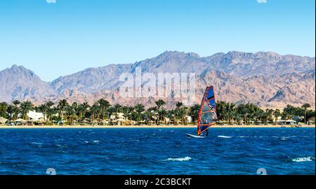 Windsurfer reitet im Meer auf dem Hintergrund des Strandes mit Palmen und hohen felsigen Bergen Stockfoto