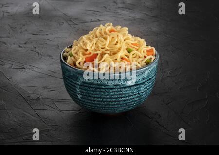 Instantnudeln mit Karotten und Hengsten, eine Schüssel Soba mit Gemüse auf schwarzem Hintergrund Stockfoto