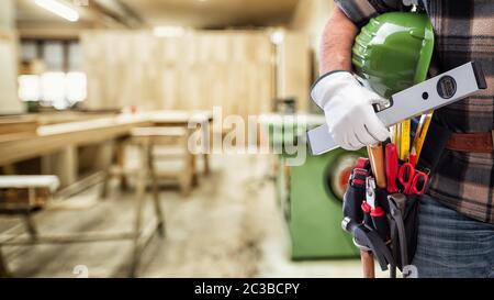 Close-up. Tischler mit Händen durch Handschuhe geschützt hält Helm und Niveau. Bauindustrie, Tischlerei. Stockfoto