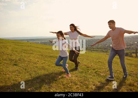 Eine positive Familie läuft fröhlich über das Feld Hände zur Seite in der Morgendämmerung in der Sonne. Stockfoto