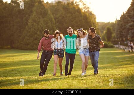 Eine Gruppe von Freunden umarmt sich während ihres Spaziergangs in der Landschaft am Sommertag. Fröhliche Leute, die ihr Wochenende draußen genießen Stockfoto