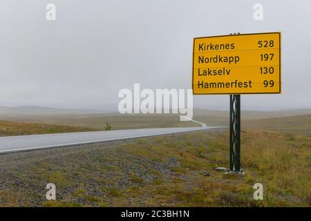 Nasse und neblige Straße mit Straßenschild in Nordnorwegen, die nach Nordkapp und anderen Orten führt. Stockfoto