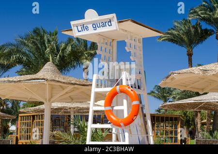 Hölzerner Rettungsschwimmer Turm mit orangefarbener Rettungsboje am Strand vor dem Hintergrund von Palmen und Schilf Stockfoto
