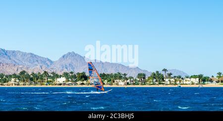 Windsurfer reitet im Meer auf dem Hintergrund des Strandes mit Palmen und hohen felsigen Bergen Stockfoto