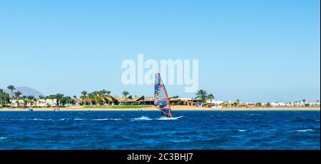 Windsurfer reitet im Meer auf dem Hintergrund des Strandes mit Palmen und hohen felsigen Bergen Stockfoto