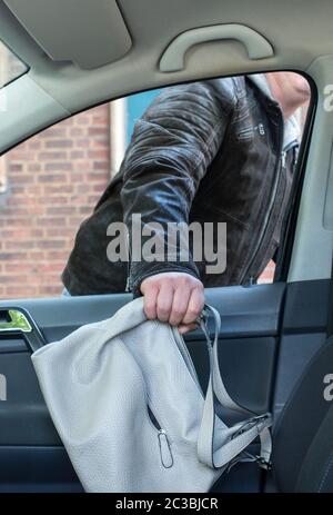 Ein Dieb stiehlt einen Geldbeutel aus einem offenen Fenster in einem Auto Stockfoto