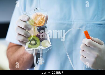 Männlicher Arzt Holding Kochsalzlösungsbehälter mit Fruchtschnitten im Inneren im Krankenhaus Stockfoto