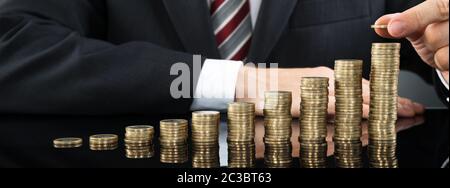 Nahaufnahme der Geschäftsmann Inverkehrbringen Münze über Stapel von Münzen am Schreibtisch Stockfoto