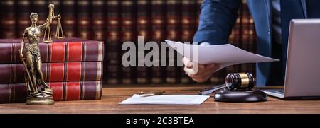 Mittelteil der Rechtsanwalt Holding Dokumente in der Nähe von Hammer und Laptop am Schreibtisch im Gerichtssaal Stockfoto