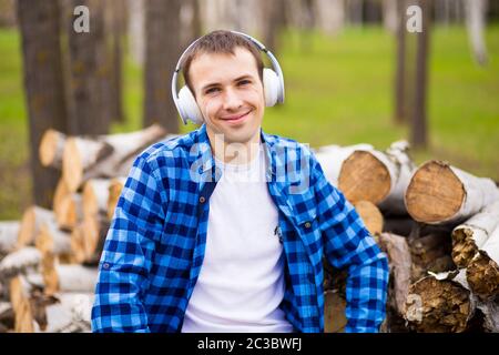 Glücklicher Mann mit Kopfhörern, der Musik hört und Smartphone-Kontrolle beim Spaziergang im Stadtpark Stockfoto