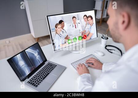 Reife männliche Arzt untersuchen Knie X-ray In der Klinik während der Videokonferenz Stockfoto