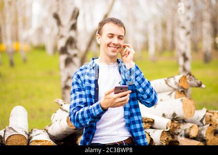 Glücklicher Mann mit Kopfhörern, der Musik hört und Smartphone-Kontrolle beim Spaziergang im Stadtpark Stockfoto