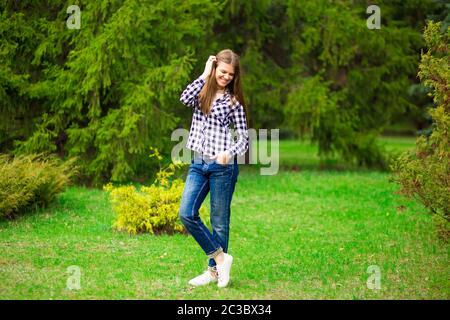 Junges Mädchen geht entlang in weißer Jacke und Jeans durch Sommerpark Stockfoto