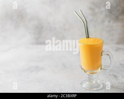 Gelbe mango Joghurt oder Smoothie auf grauem Zement Hintergrund mit Kopie Raum gelassen. Gelbwurz Lassie oder Lassi in Glas mit Metall Strohhalme Stockfoto