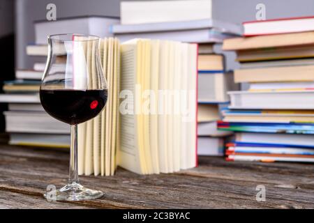 Buch und Weinglas vor Stapeln verschiedener Bücher auf Holztisch Stockfoto