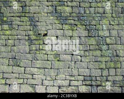 Eine alte graue Steinwand aus großen unregelmäßigen Blöcken, die mit Moosmustern bedeckt sind Stockfoto