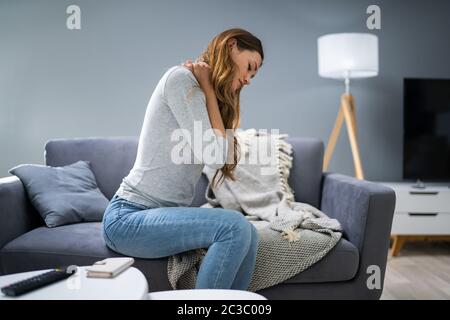 Reife Frau in Neckache beim Sitzen auf dem Sofa Stockfoto