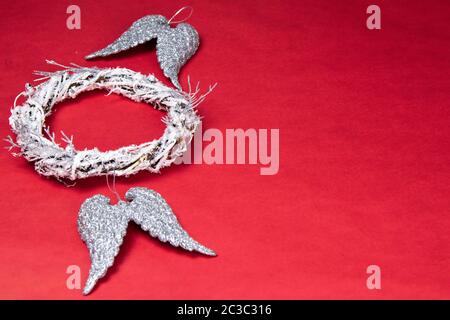 Eine Tür Kranz aus Zweigen verziert mit künstlichen Schnee. In der Nähe befinden sich Engel Flügel der silberne Farbe. Alles steht auf einem roten Hintergrund mit einem Platz f Stockfoto