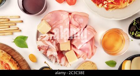 Italienische Charcuterie, ein flaches Panorama. Eine Auswahl an Schinken und Käse, von oben auf weißem Hintergrund mit Wein gla geschossen Stockfoto