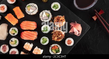 Großes Sushi-Set-Panorama mit Sojasauce und Essstäbchen, von oben auf schwarzem Hintergrund aufgenommen. Eine Auswahl an verschiedenen Maki, ni Stockfoto
