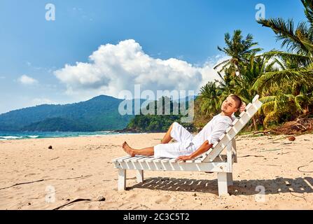 Mann in Weiß, der sich in der Sonnenliege am Strand entspannt Stockfoto