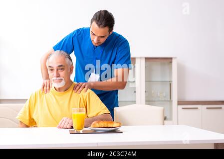 Junger männlicher Arzt besucht zu Hause den alten Patienten Stockfoto