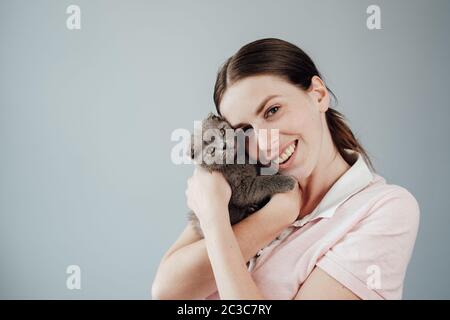 Studio Portrait von Young Adult Pretty Girl in Rosa T-Shirt Hugs ihre kleine schottische Falte Katze gekleidet Stockfoto