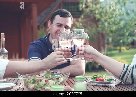 Glückliche Freunde, die mit Gläsern beim Abendessen am Tisch im Garten klimmten Stockfoto