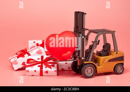 Gabelstapler, rotes Herz und Geschenkboxen auf rosa Hintergrund. Valentinstag. Hochzeitstag Stockfoto