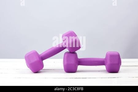 Zwei violette Kunststoff-Hanteln für Sport auf weißem Holzhintergrund, Kopierraum. Fitness-Training. Gesunder Lebensstil. Stockfoto