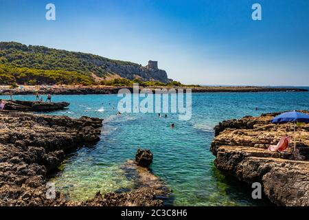 20. August 2019 - Nardò, Italien, Apulien, Salento - Bucht von Porto Selvaggio. Kiesstrand und felsiger Strand. Die Menschen sonnen sich und schwimmen im türkisfarbenen Meer. Das T Stockfoto