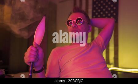 Hipster Mann rauchen Shisha in rosa Farbe Beleuchtung in dunklen Raum mit Neonlicht. Abstraktes unfokussierte Bild Stockfoto