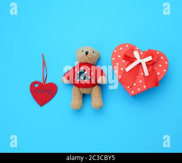 Roter Pappkarton in Form eines Herzens und kleiner brauner Teddybär auf hellblauem Grund, Draufsicht Stockfoto
