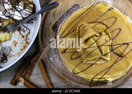 Karamellisierte Äpfel mit Honig und Zimt in einer Tonschale und Pfannkuchen mit Butter und Schokolade auf hellem Holzhintergrund. Draufsichten Stockfoto