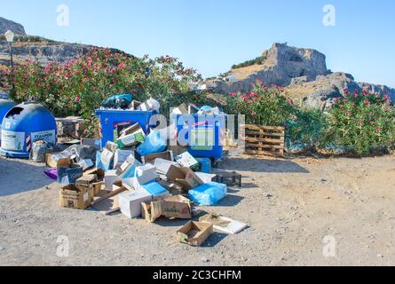 LINDOS (INSEL RHODOS), GRIECHENLAND – 8. AUGUST 2019: Müllhaufen auf dem Boden in der Nähe von Plastikmüll auf dem Parkplatz. Akropolis von Lindos im Hintergrund Stockfoto