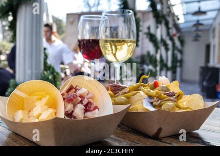 Tapas-Bar. Käse, Schinken und Pinchos mit Paprika, mit Brille Rot- und Weißwein auf einem Holztisch in einem Café im Freien Stockfoto