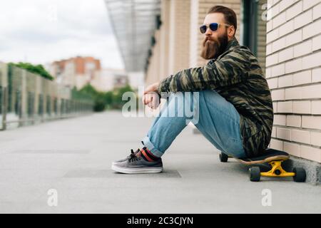 Schöner junger Mann, der auf dem Longboard auf der Straße in der Stadt sitzt. Urban Skateboarding Konzept. Stockfoto