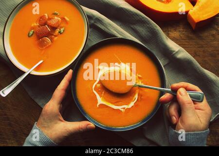 Flachbild-lay von weiblichen Händen und Fall Erwärmung Kürbis creme Suppe mit Croutons und Samen an Bord über rustikal Hintergrund, Ansicht von oben. Herbst vegetari Stockfoto