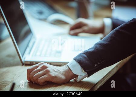 Gut gekleideter Geschäftsmann verwendet Laptop-Computer, während er am Arbeitsplatz im Büro arbeitet. Fokus auf männliche Hand im Vordergrund. Nahaufnahme. Getönt Stockfoto