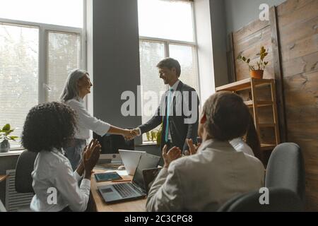 Geschäftsleute schütteln die Hände. Der Projektmanager schüttelt dem Mitarbeiter die Hände zum Beifall des Teams, das im Büro am Verhandlungstisch sitzt. Getöntes Bild Stockfoto