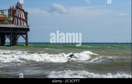 Brighton UK 19. Juni 2020 - Surfer versuchen an einem sonnigen, aber luftigen Nachmittag entlang der Südküste eine Welle am Brighton Palace Pier zu fangen. Das Wetter wird voraussichtlich viel wärmer werden nächste Woche mit Temperaturen voraussichtlich 30 Grad in Teilen des Südostens erreichen : Credit Simon Dack / Alamy Live News Stockfoto