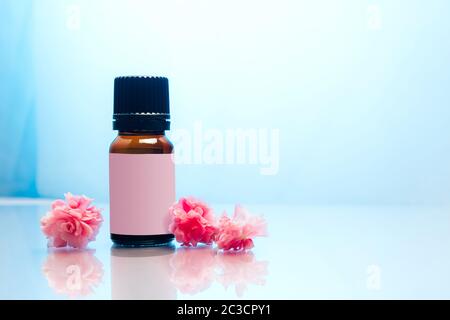 Flasche ätherisches Öl mit rosa Blüten auf blauem Hintergrund. Stockfoto