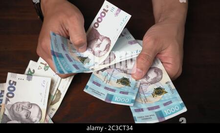 Kaukasischer Mann hält neue ukrainische Papiergeld. Männliche Hände halten Packung von Banknoten Nennwert 1000 Griwna. Nahaufnahme Stockfoto