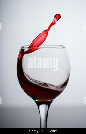 Spritzer Rotwein in einem Glas auf einem schwarzen glänzendem Glas auf weißem Hintergrund Stockfoto